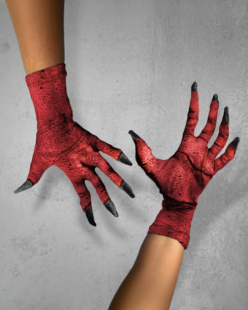 A pair of fabric printed red stone-like clawed gloves worn on hands. They look like stone or course skin, shown against  textured gray background. The gloves have a distressed, red color with spattered black spots of and pointy black claws on the fingers.