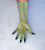 A long, fitted glove or sleeve worn on a hand, shown against a light textured background. The glove is a muted olive green with black gradient tips on the fingers.