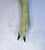 A single long green glove or sleeve worn on a hand, shown against a light textured background. The glove is olive green with two black-tipped fingers in an upside down peace sign. Palm down