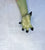 A single long green glove with black claw-like tips, worn on a visible forearm, photographed against a light textured background.Hand reaches toward the camera