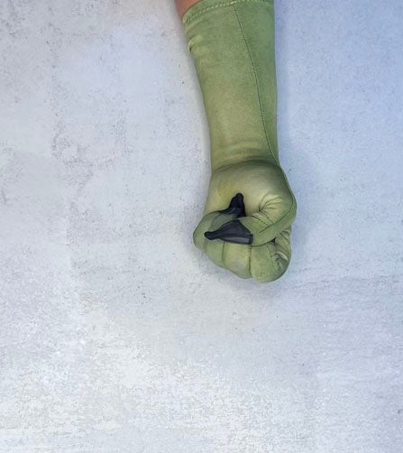A single long green glove on a hand, shown in a fisted grip against a light textured background. The glove is olive green. 