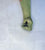A single long green glove on a hand, shown in a fisted grip against a light textured background. The glove is olive green. 